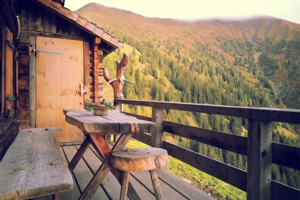 Balcon en bois d'un chalet avec table et bancs, face aux collines boisées